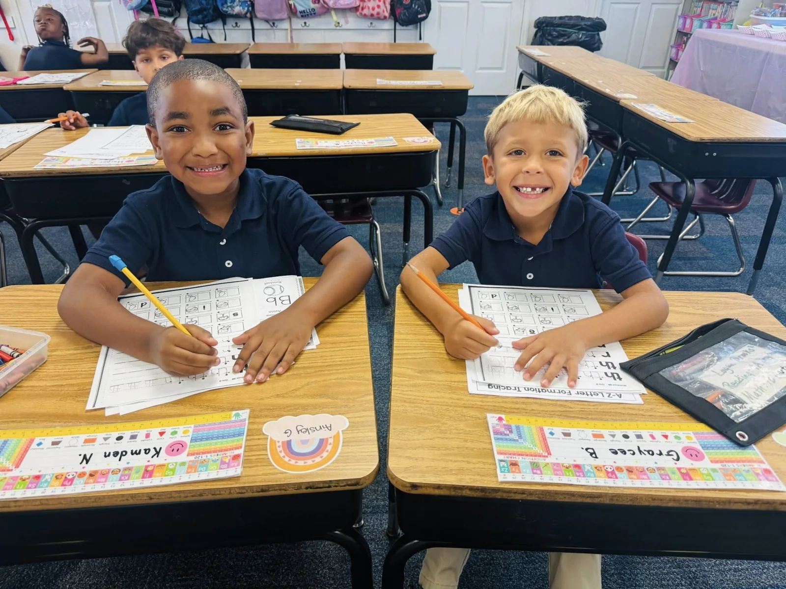 Two smiling students work together at their classroom desks.