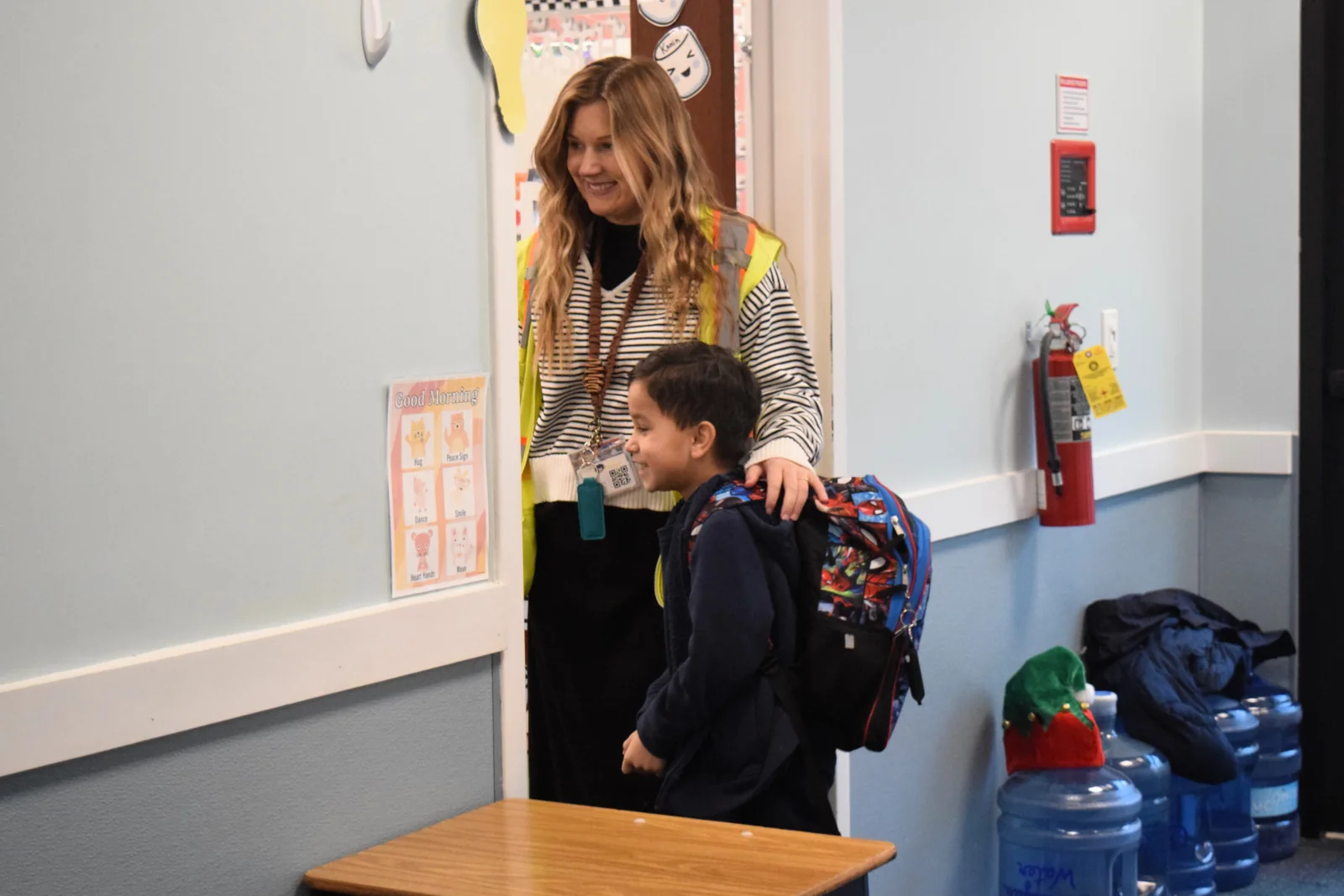 A teacher welcomes children into a classroom.