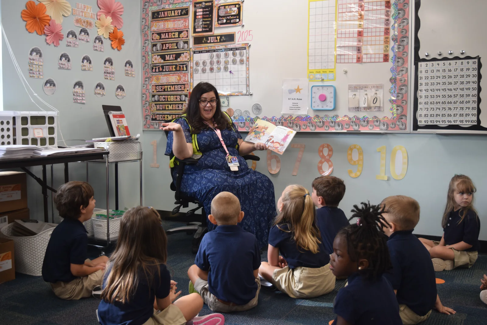 A teacher reads to students gathered on the classroom floor.